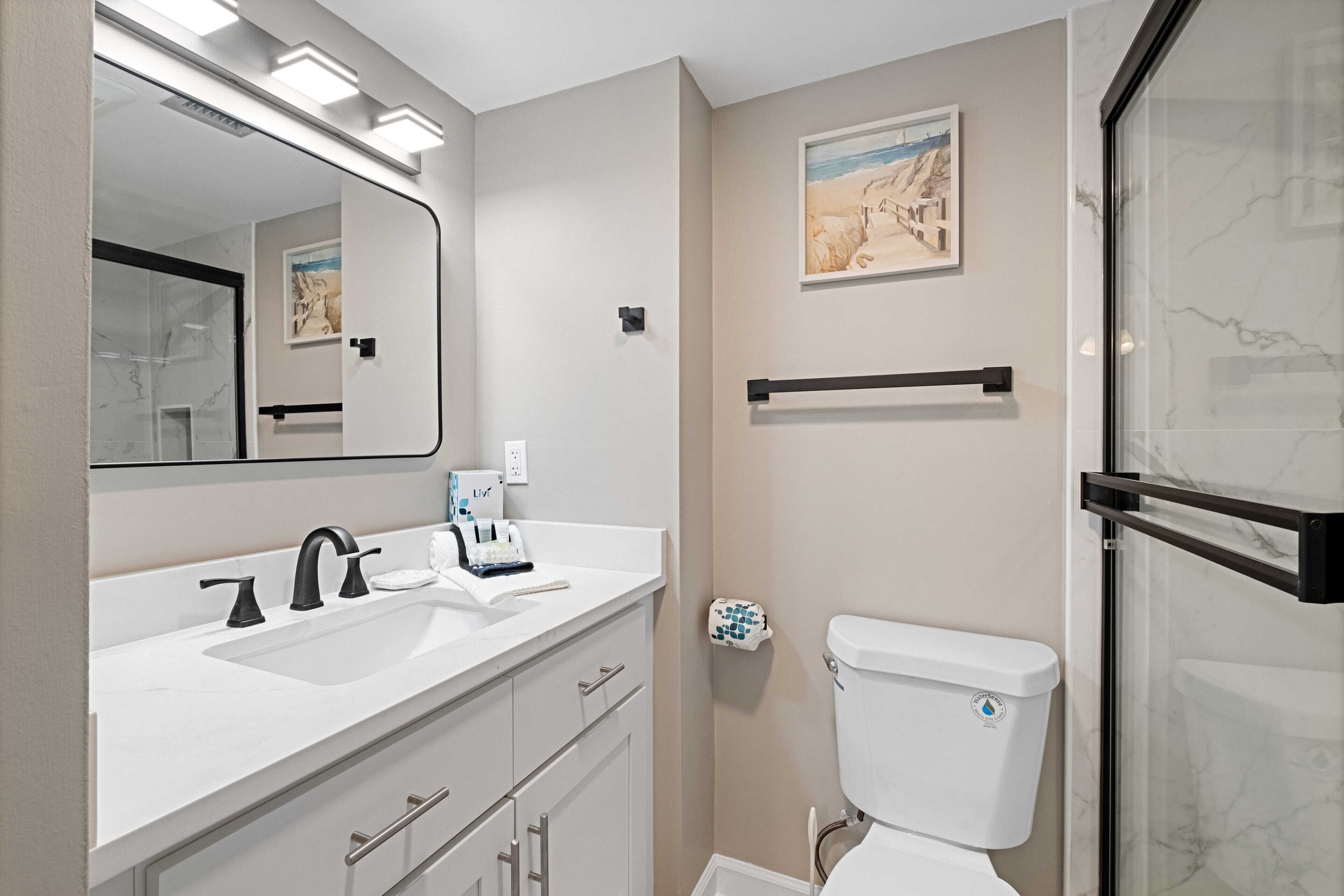 A modern bathroom with a white sink, black faucet, and a toilet with a marble surround.