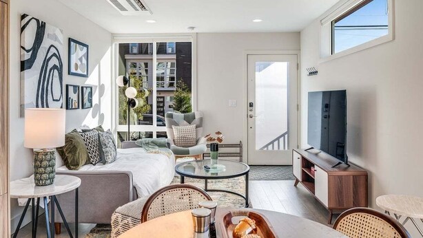A modern living room with a sofa, coffee table, and TV. There is a balcony with plants and a view of buildings. - Perch - Dayton Dream: Cozy and Modern Home | Parking and City View (Seattle)