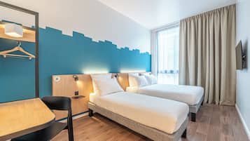 Habitación de hotel con dos camas, un escritorio, una silla, una mesa de madera, una lámpara colgante y un ventanal con cortinas.