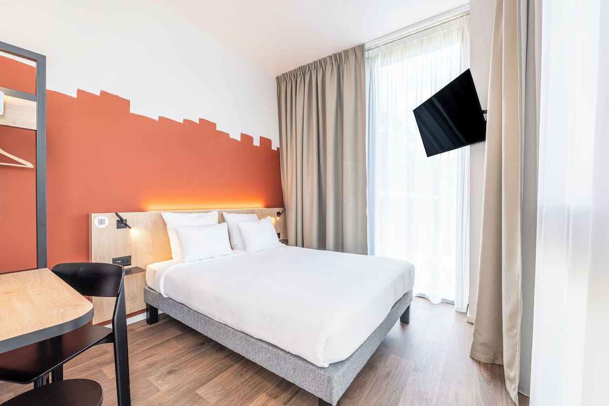 Hotellihuone, jossa on sänky, työpöytä, tuoli, seinälle asennettu televisio ja ikkuna, jossa on verhot.