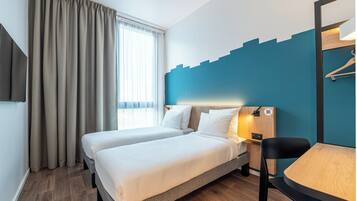 A hotel room with two beds, a desk, a chair, a TV, and a window with curtains.