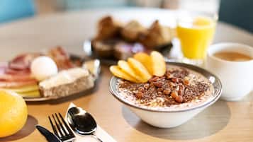 Mesa de café da manhã com tigela de cereal coberta com nozes e frutas, pão com ovos e um copo de suco de laranja.