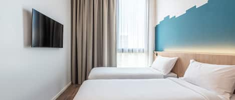 A hotel room with two beds, a flat-screen TV mounted on the wall, and a large window with curtains.