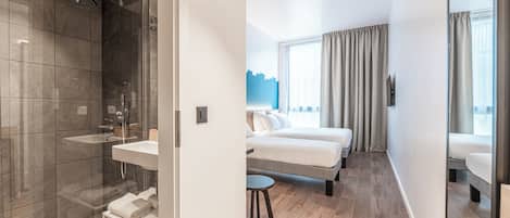 Et moderne hotelværelse med brusebad, vask, seng, et lille bord og et vindue med gardiner.