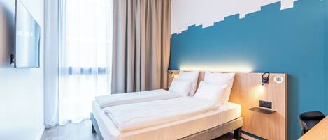 Una habitación de hotel moderna con una cama grande, un televisor de pantalla plana montado en la pared y una mesita de noche de madera.