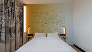 Habitación de hotel con una cama grande, dos mesitas de noche con lámparas y un papel tapiz estampado.