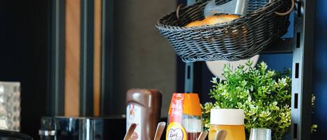 A kitchen counter with various food items, including jars of preserves, a bottle of ketchup, and a basket with bread.