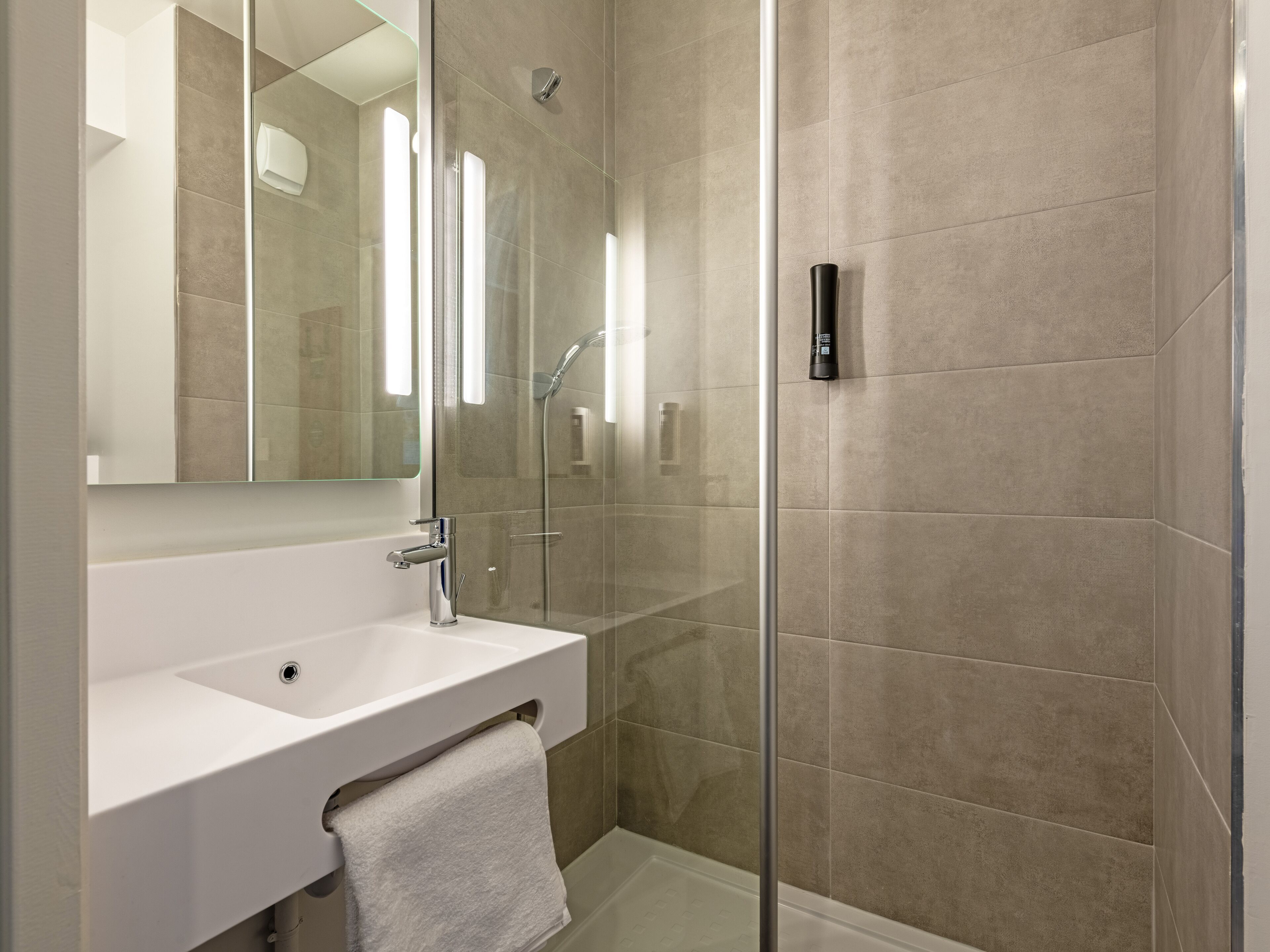 A modern bathroom with a glass-enclosed shower, a white sink, and a large mirror.