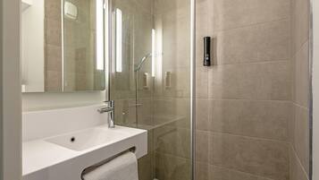 Un baño moderno con ducha de vidrio, un lavamanos blanco y un espejo grande.
