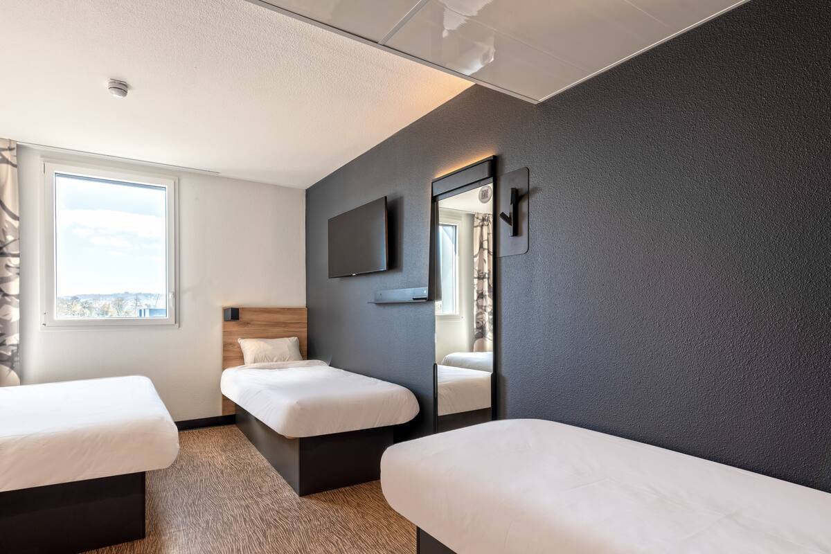 Een moderne hotelkamer met twee enkele bedden, een grote spiegel, een flatscreen televisie en een raam met uitzicht op de stad.