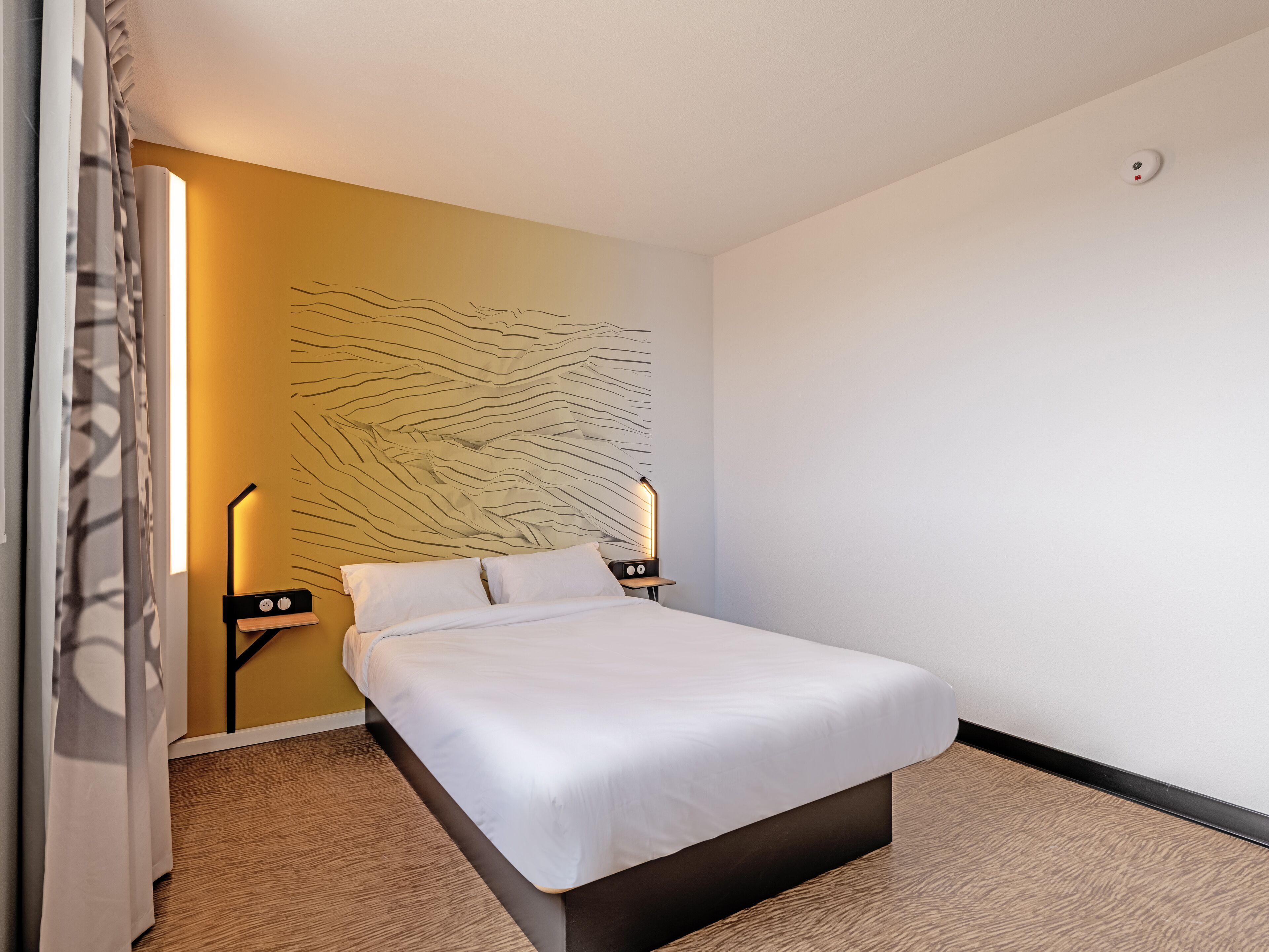 Una habitación de hotel con una cama, una lámpara de pared y una lámpara en el techo.