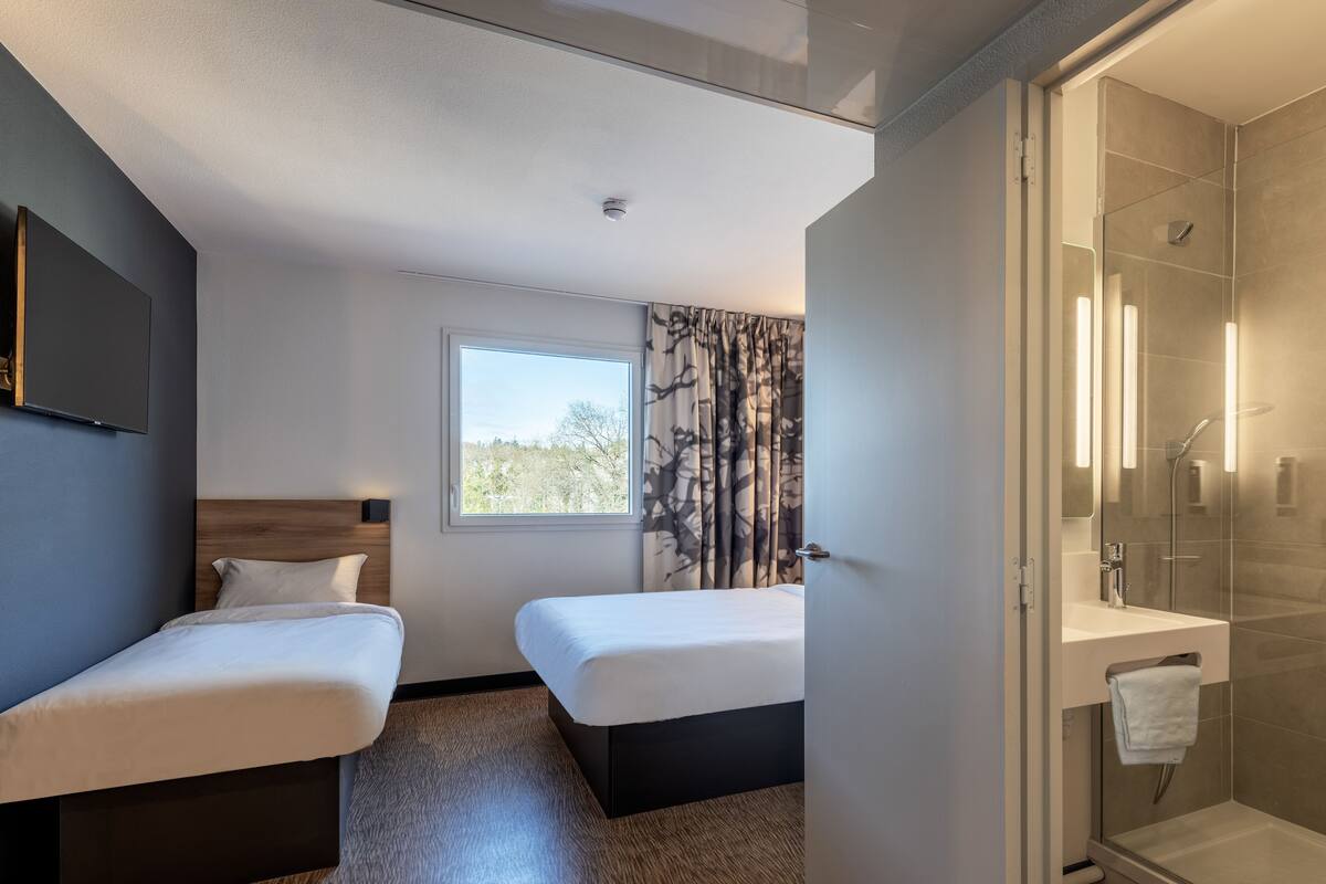 Een hotelkamer met twee enkele bedden, een groot raam met uitzicht, een douche en een wandtelevisie.