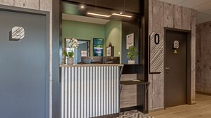 Zona de recepción con mostrador, planta en maceta, escritorio con computadora y puerta con letrero.