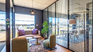 Un interior moderno con un sofá, sillas, una planta en maceta y vistas al exterior.