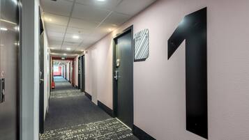 A hotel hallway with doors, a fire extinguisher, and a carpet with text.