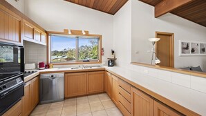 A modern kitchen with wooden cabinets, a stainless steel dishwasher, a black oven, and a window with a view of greenery. - 22 Golf Links Road (Anglesea)