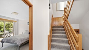 A bedroom with a bed, a wooden staircase, and a view of trees through a window. - 22 Golf Links Road (Anglesea)