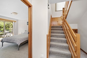Une chambre à coucher avec un lit, un escalier en bois et une vue sur les arbres par la fenêtre.