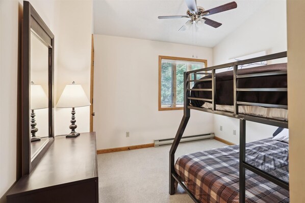 A bunk bed room with a ceiling fan, a window with blinds, a lamp, and a mirror.