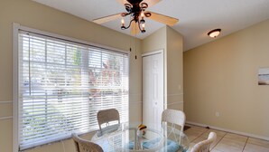 A dining area with a glass table surrounded by wicker chairs, a ceiling fan, and a view through large windows. - Bright Titusville Retreat w/ Lanai - WFH Friendly! (Titusville)