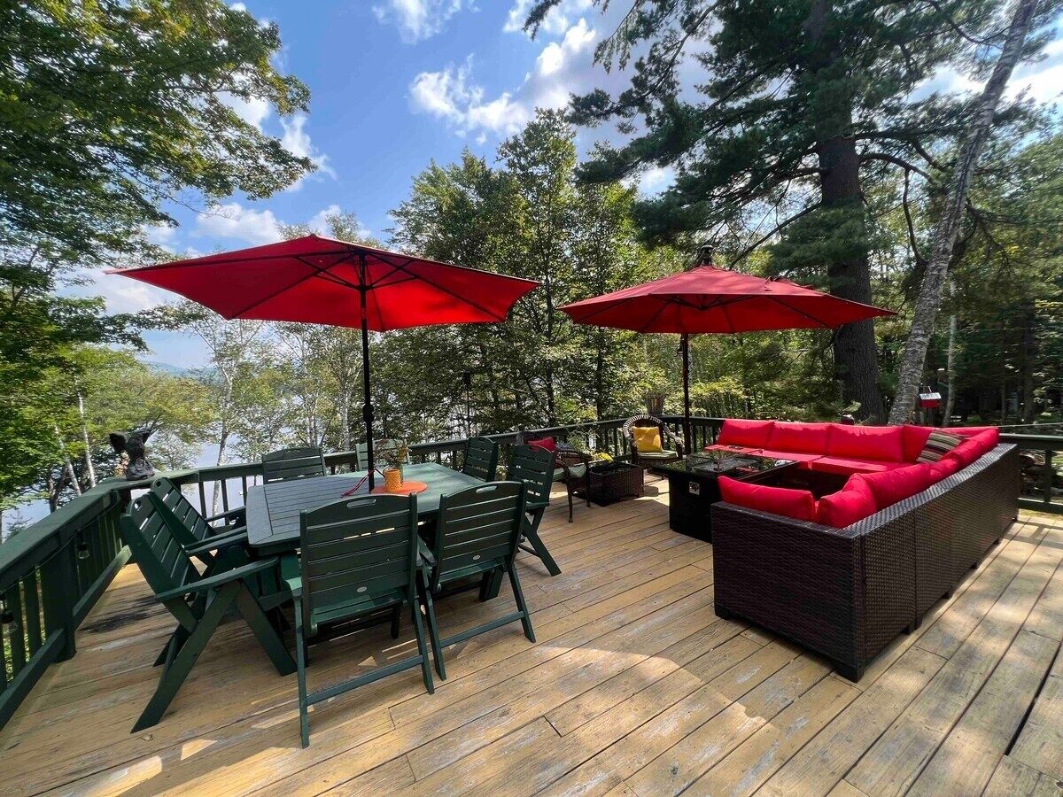 Una terraza con mesa y sillas, sombrillas rojas y un sofá con cojines rojos.
