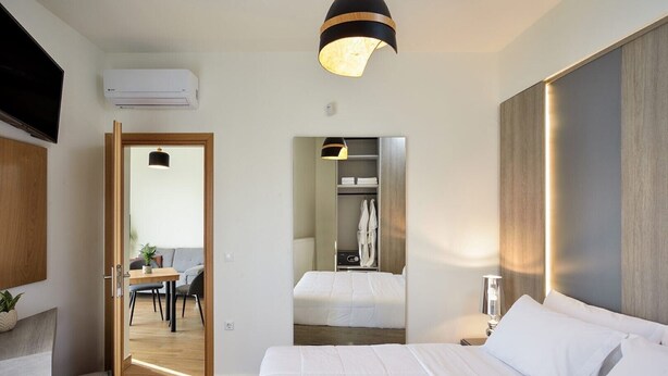 Une chambre d’hôtel avec un lit, une table de chevet et un miroir. Une porte donne accès à un coin repas, où se trouvent une table et des chaises.