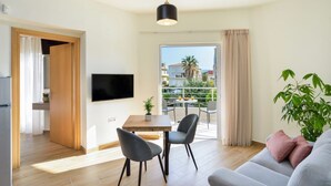 Un salon moderne avec un téléviseur à écran plat, une table à manger en bois, deux chaises, un canapé gris et une plante en pot.