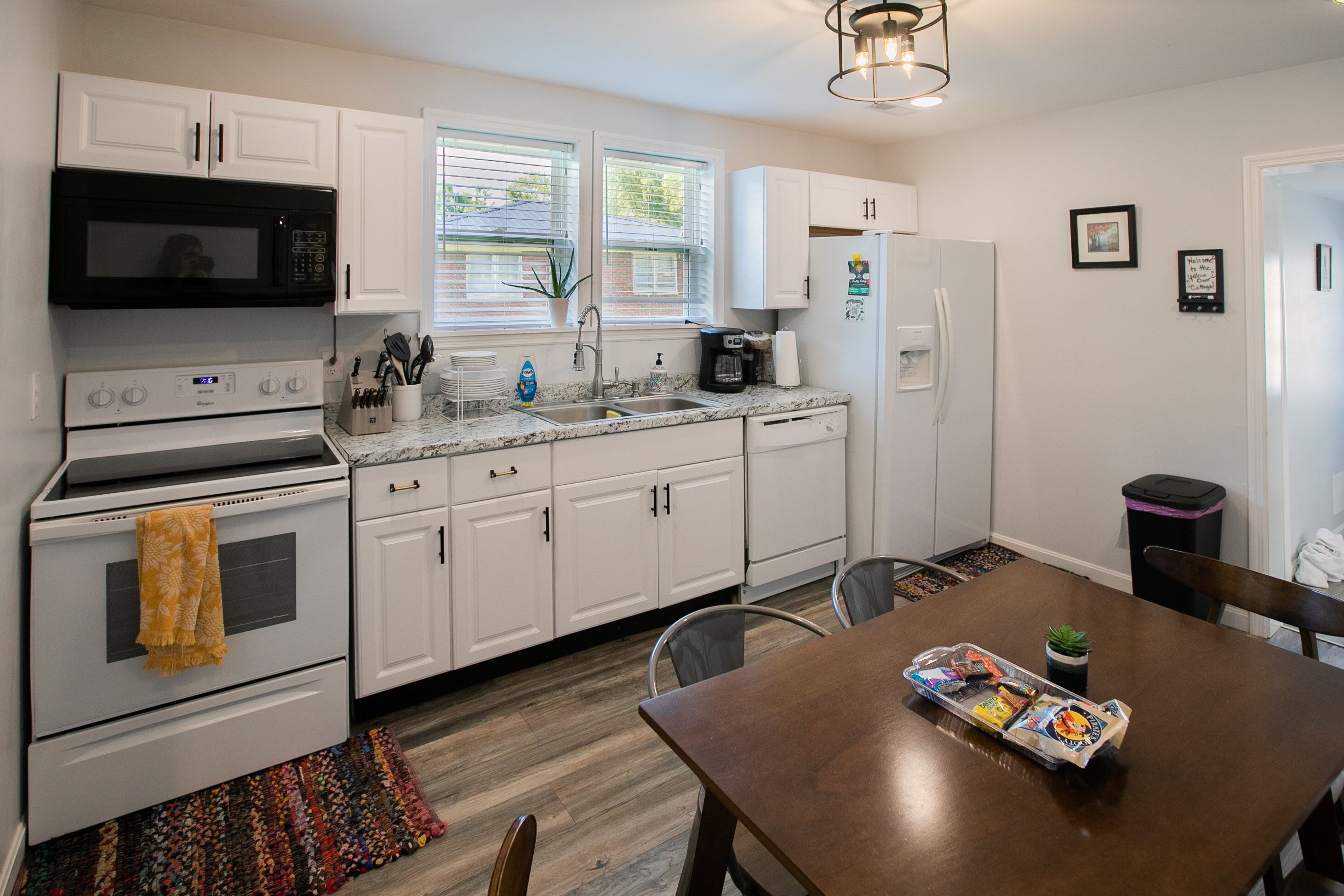 A modern kitchen with white cabinets, a stainless steel oven, a microwave, a sink, and a dining table with chairs.