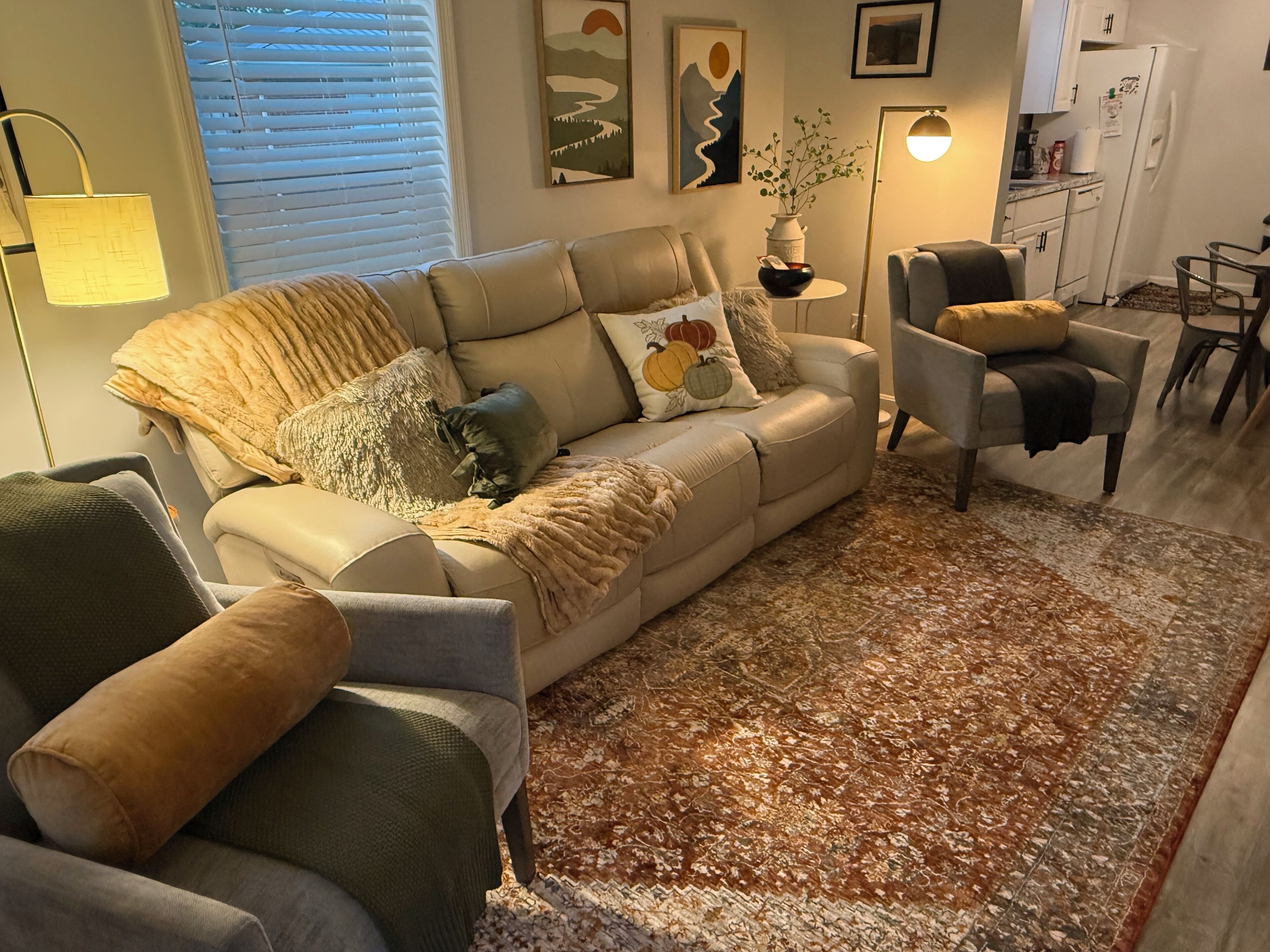 Ein Wohnzimmer mit einem beigen Sofa, einem gemusterten Teppich und einem kleinen Beistelltisch mit einer Vase.