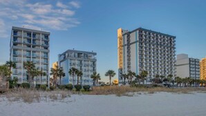 A beachfront hotel with multiple-story buildings, balconies, and palm trees.