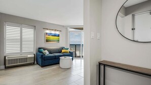 A modern living room with a blue sofa, a round mirror, and a view of the sea through a sliding glass door.