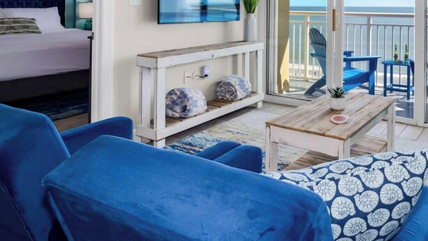 Una propiedad frente a la playa con balcón, una cama, muebles azules y televisor.