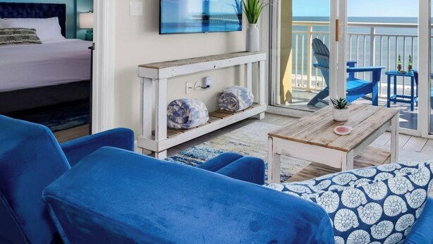 A beachfront property with a balcony, a bed, blue furniture, and a television.