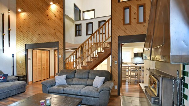 A spacious living area with a wooden staircase, a sofa, and a fireplace. - Fully equipped Blue Mountain Chalet with outdoor hot tub (Town of the Blue Mountains)