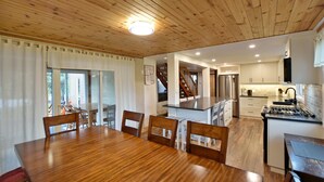 A modern kitchen with a central island, wooden dining table, and chairs. - Fully equipped Blue Mountain Chalet with outdoor hot tub (Town of the Blue Mountains)