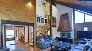 A spacious living area with a wooden ceiling, a staircase, a fireplace, and a television. - Fully equipped Blue Mountain Chalet with outdoor hot tub (Town of the Blue Mountains)