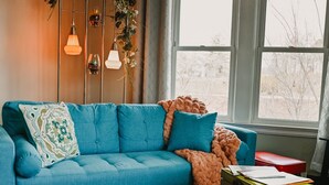 A cozy living room with a blue sofa, a red ottoman, a green chest of drawers, and a patterned rug.