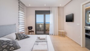 Ein modernes Hotelzimmer mit Bett, Fernseher, Balkon mit Meerblick und einem kleinen Tisch mit Stühlen.