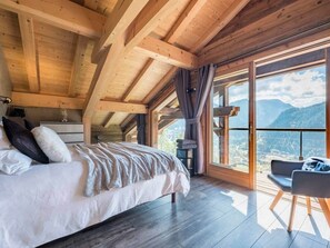 A bedroom with a large bed, a chair, and a view of mountains through large windows. - Chalet Prestige Le Spencer - Spa & panoramic view (Châtel)