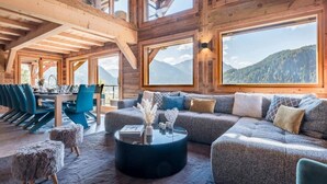 Ein geräumiges Zimmer mit einer großen Couch, einem Esstisch mit Stühlen und Bergblick durch große Fenster.