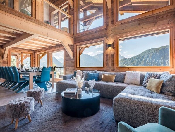 A spacious room with a large sofa, a dining table with chairs, and a view of mountains through large windows. - Chalet Prestige Le Spencer - Spa & panoramic view (Châtel)