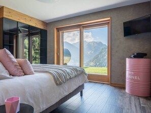 A bedroom with a bed, a large window, a TV, and a Chanel barrel.