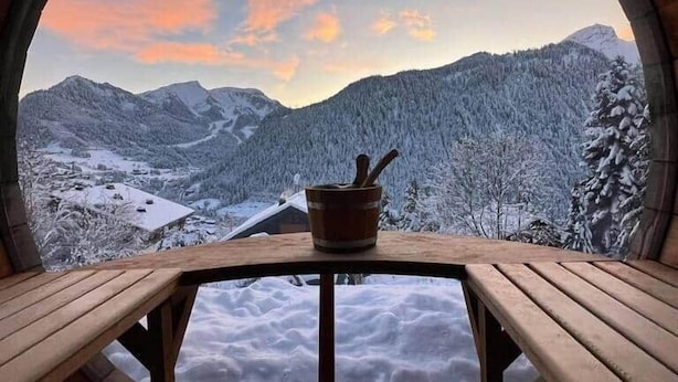 Ein runder Holzraum mit Tisch und Bänken, mit Blick auf eine verschneite Berglandschaft.
