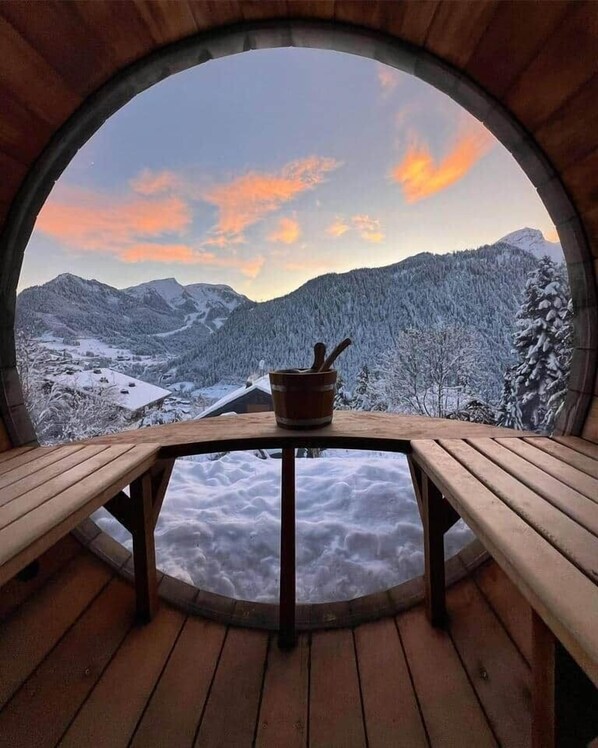 A circular wooden room with a table and benches, overlooking a snowy mountainous landscape.