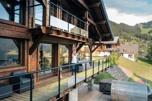 A wooden deck with outdoor seating, a glass balustrade, and a view of a mountainous landscape. - Chalet Prestige Le Spencer - Spa & panoramic view (Châtel)