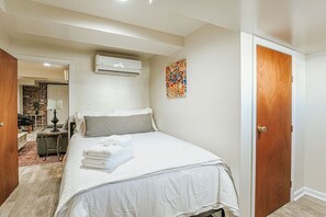 Quarto com cama, ar condicionado, porta de madeira e uma obra de arte colorida na parede.