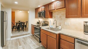 Una cocina moderna con armarios de madera, encimera de granito, electrodomésticos de acero inoxidable y un comedor con mesa y sillas.
