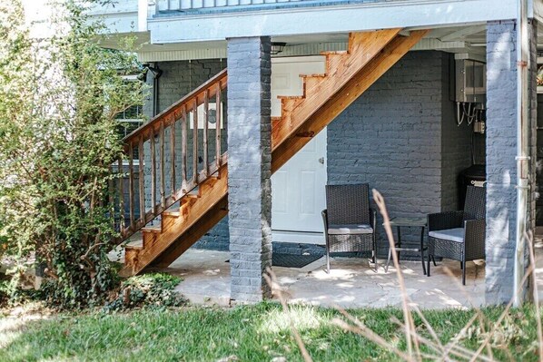 A covered outdoor area with a wooden staircase, stone pillars, and wicker furniture.