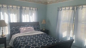 A bedroom with a bed, a nightstand, a lamp, and curtains. - Cozy Studio apartment with cabin feel (Tallahassee)