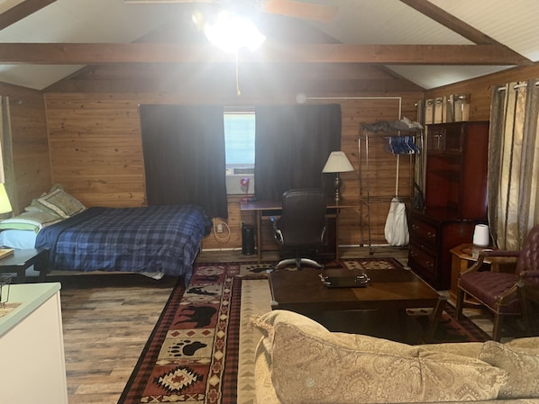 A cozy room with a bed, a desk, a chair, and a sofa. There is a window with curtains and a ceiling fan.